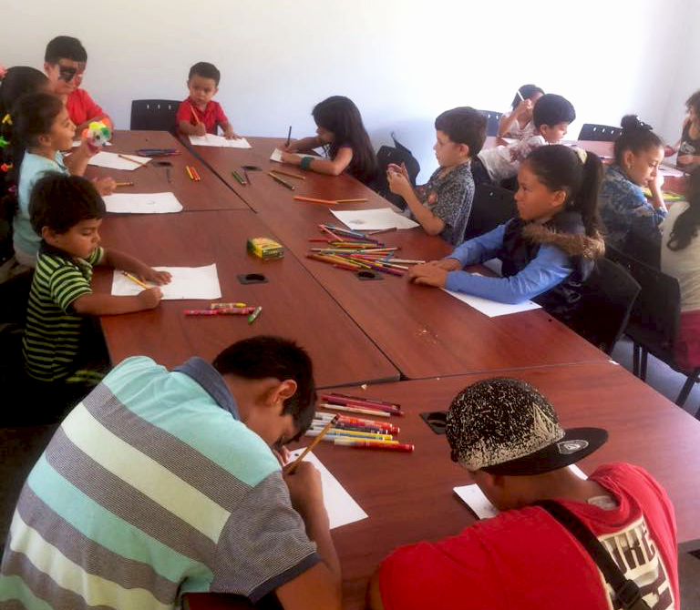 Jóvenes se reunen alrededor de una mesa para dibujar.