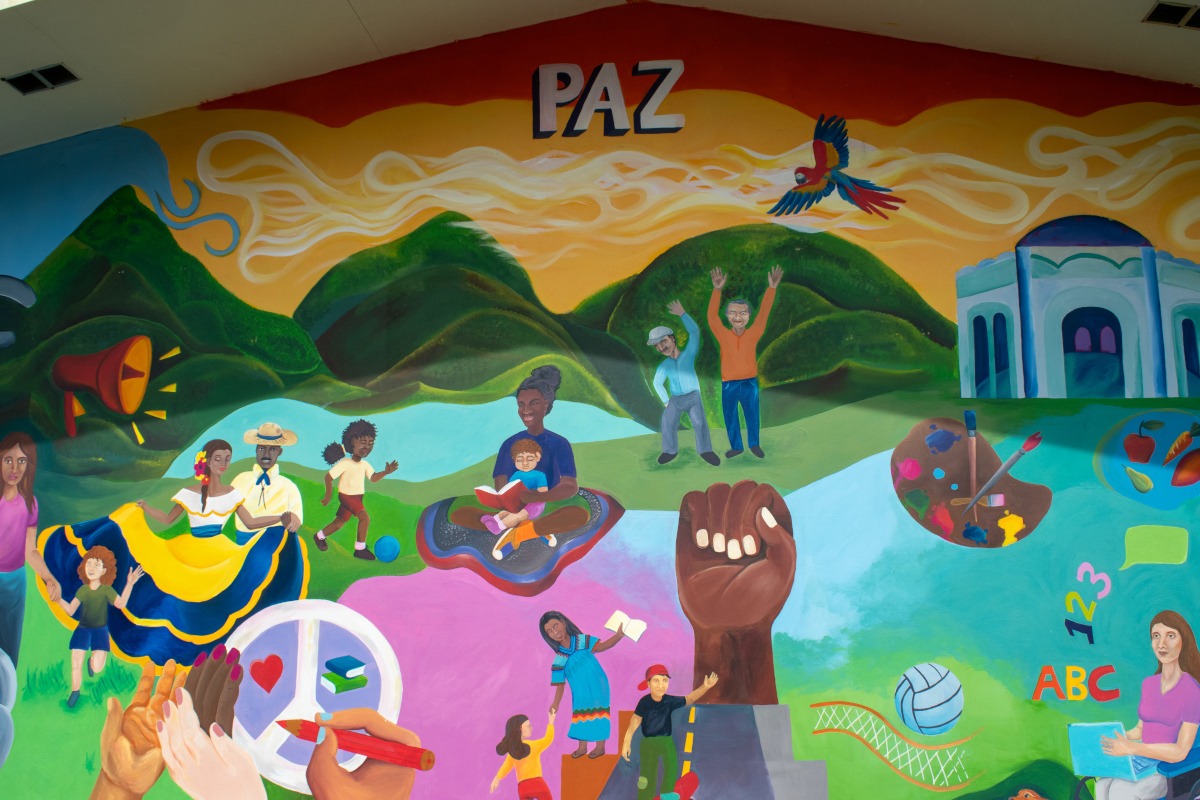 Mural pintado de varios colores que incluye la flora y fauna, las ciencias y el arte, todos los elementos conviviendo con las personas de la comunidad